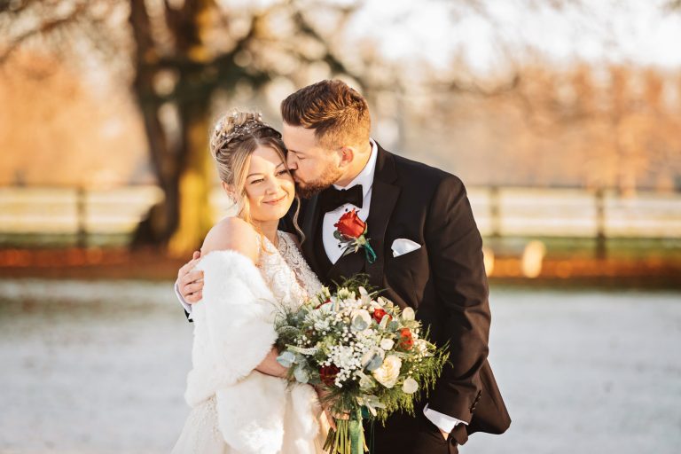 A groom hugs and kisses his bride in the golden hour at Eastington Park