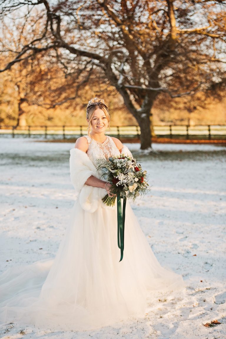 A bride stands in the golden hour in the snowy grounds at Gloucestershire wedding venue, Eastington Park.