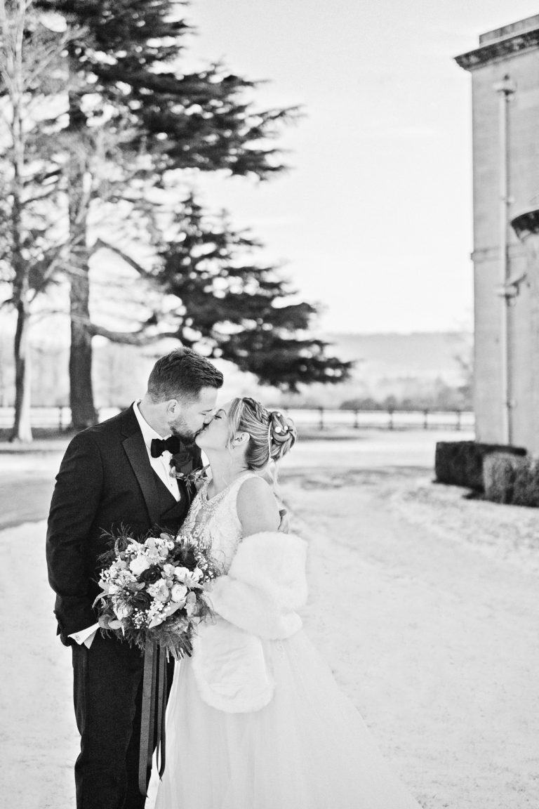 B&W portrait of bride and groom kissing in the wintery grounds of Eastington Park.
