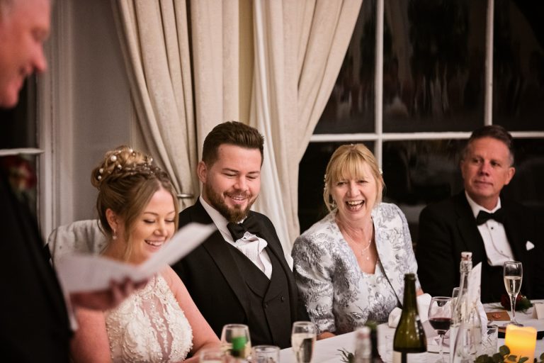 The wedding top table smile and laugh at the father of the brides speech. Photograph by Blooming Photography taken at Eastington Park at Christmas Wedding.