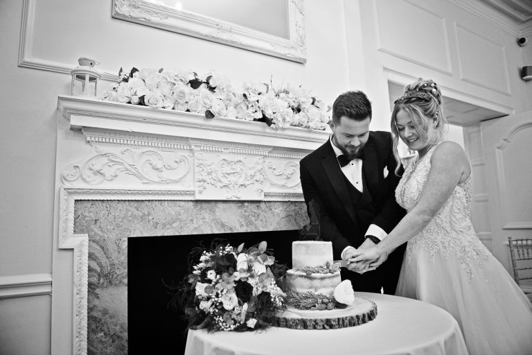 Bride and groom cut their wedding cake next to a fire place at Eastington Park for a Christmas Wedding.