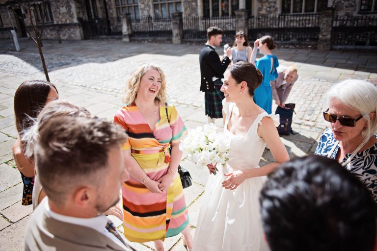 Guests laughing with bride outside Winchester Registry office wedding. Candid photo by Blooming Photography