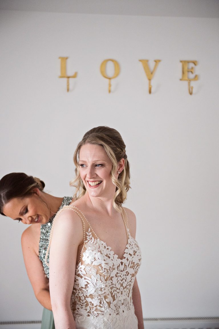 Documentary photo of bride having her wedding dress done up. LOVE letters behind.
