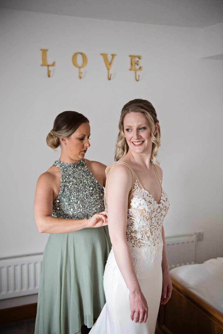 Documentary photo of bride having her wedding dress done up.