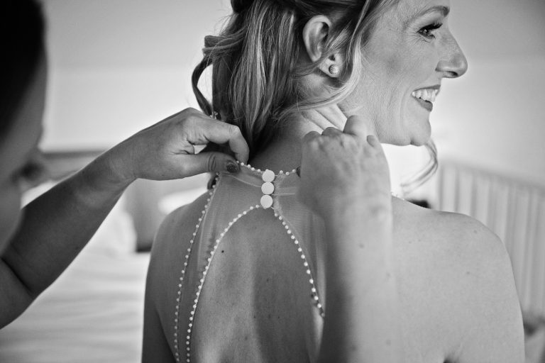 Documentary b&w photo of bride having her wedding dress done up.