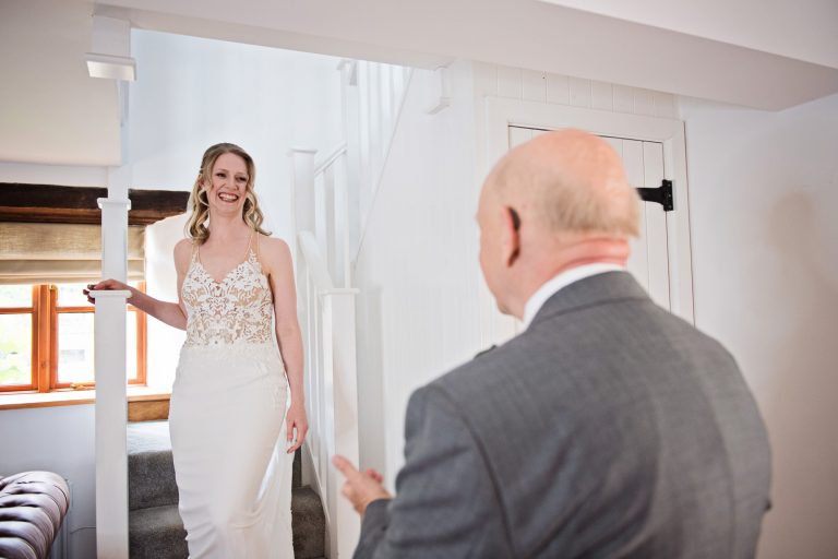 Bride walking down the stairs to see her dad for the first time in her wedding dress.