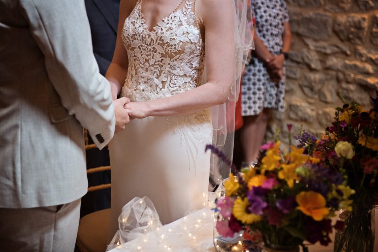 Close up of bride and groom holding hands.