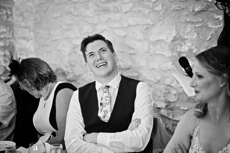 B&w photo of groom grimacing during a bestman's speech.