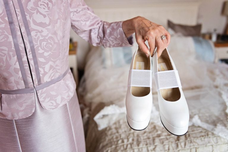 Mother of the groom holds the brides wedding shoes. Candid photograph by Blooming Photography.