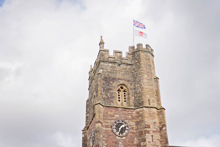 Outside of St George Parish Church, Easton-In-Gordano, cloudy day with Union Jack and Japanese flag flying.