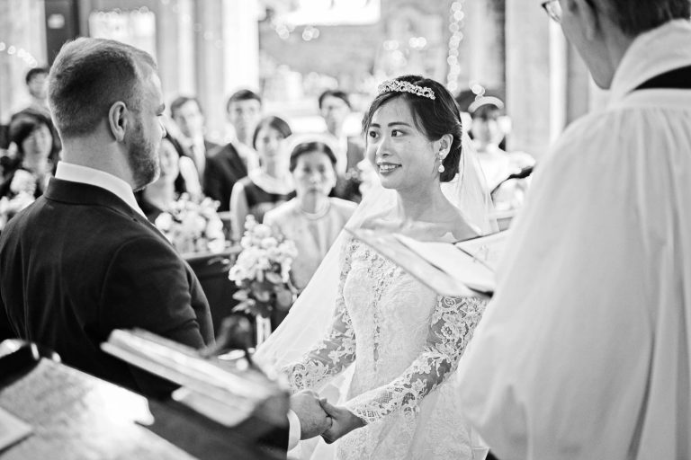 The bride and groom look at each other during the wedding ceremony. Story telling, black and white photograph by Blooming Photography.