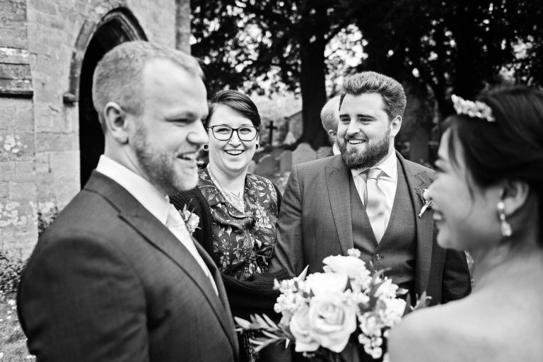 Guests chatting to the bride and groom. Candid black and white photograph by Blooming Photography.