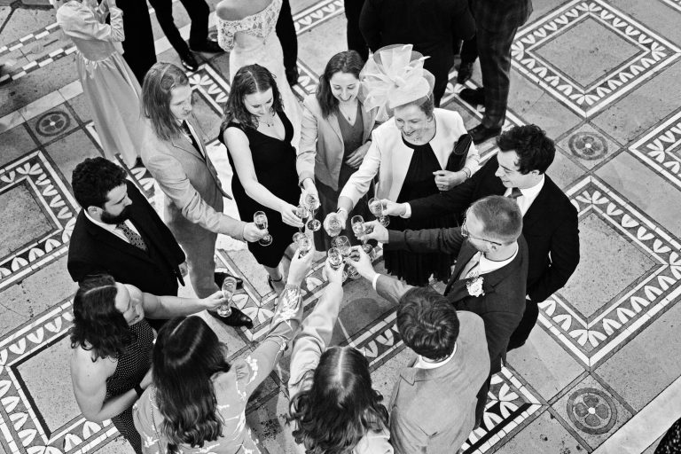 Wedding guests (11 people) gather together to do a cheers, shot from above. Amazing tiled floor at Leigh Court. Candid black and white photograph by Blooming Photography.