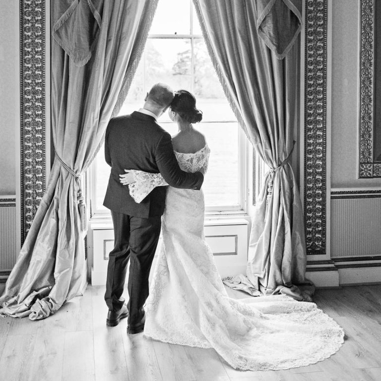 Portrait photo of Bride and groom standing together in the window of the tapestry room in Leigh Court. Candid square black and white photograph by Blooming Photography.