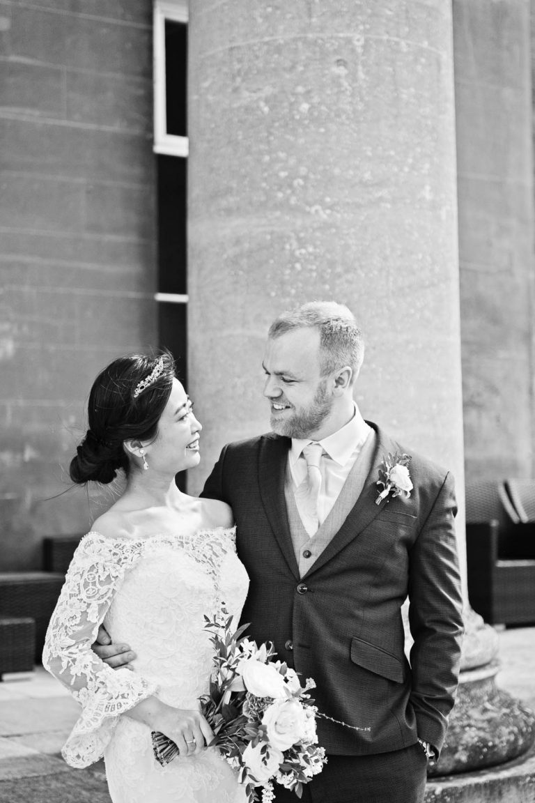 Portrait photo of bride and groom outside the pillars at Leigh Court, Bristol wedding. Candid black and white photograph by Blooming Photography.