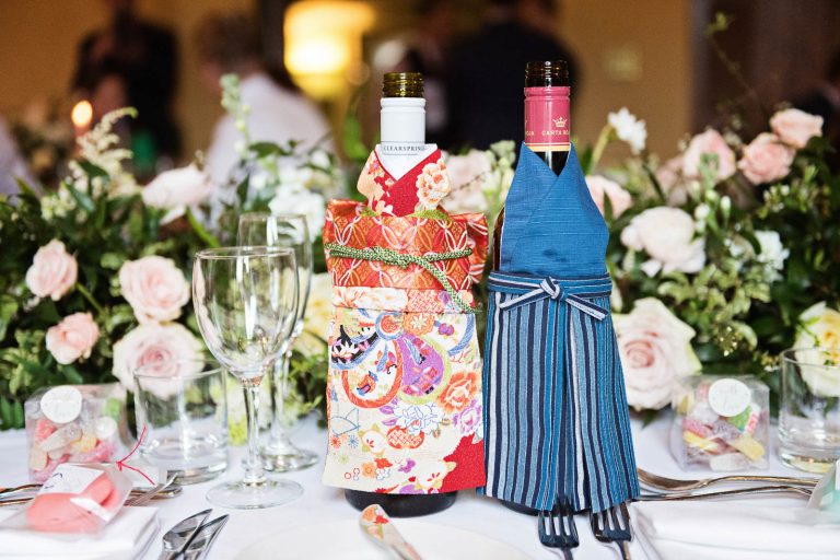 Wedding details. Japanese wine bottle coats, glasses and floral table bouquets. Photograph by Ben Roberts.