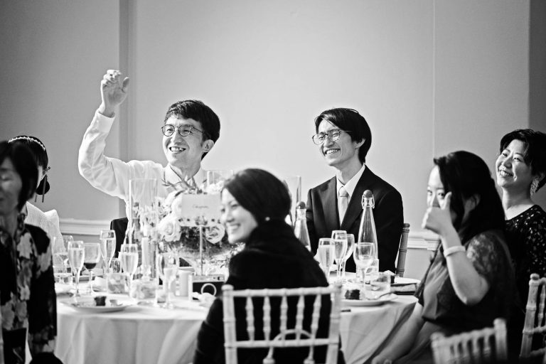 Photo of wedding guests giving the thumbs up to the Japanese translation. Black and white story telling photograph.