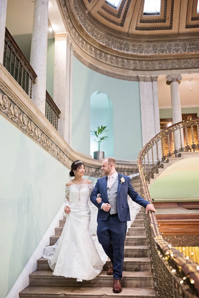 Portrait photo of Bride and groom walking down the steps in the Great Hall at Leigh Court, Bristol. Photograph by Blooming Photography