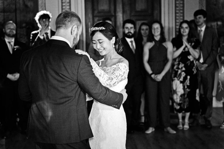 Bride and groom smile as they do the first dance. Black and white photo by Blooming Photography.
