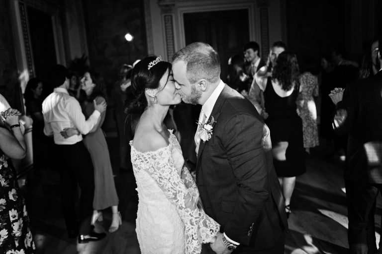 Bride and groom seal the end of the evening with a kiss. Black and white photograph by Blooming Photography.