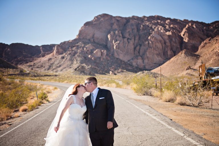 Bride and groom kiss each other along the highway in Nevada with rocks behind them Photograph by Blooming Photography, photographed at Nelson Ghost Town.