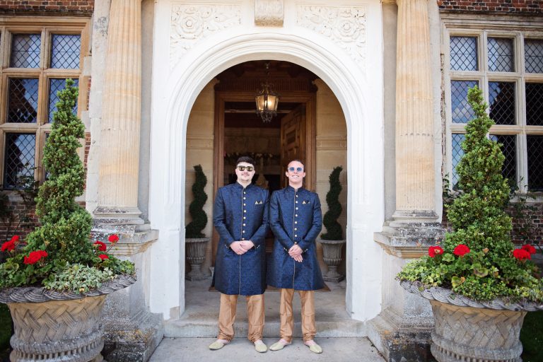Groomsmen stand at elegant door entrance at North Mymms Park, candidly photographed by Blooming Photography.