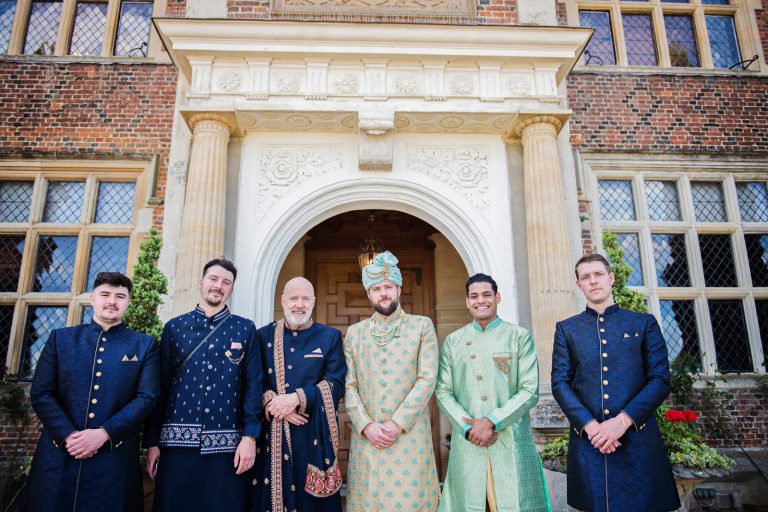 Grooms men stand outside door and arch at North Mymms Park, candidly photographed by Blooming Photography.
