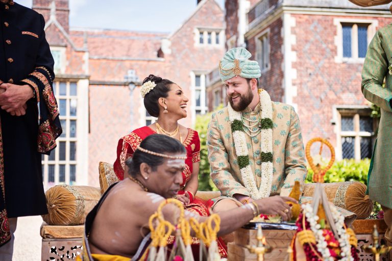 Bride and groom exchange laughter during outdoor Indian wedding ceremony. Photographed at North Mymms Park, candidly photographed by Blooming Photography. Colourful.