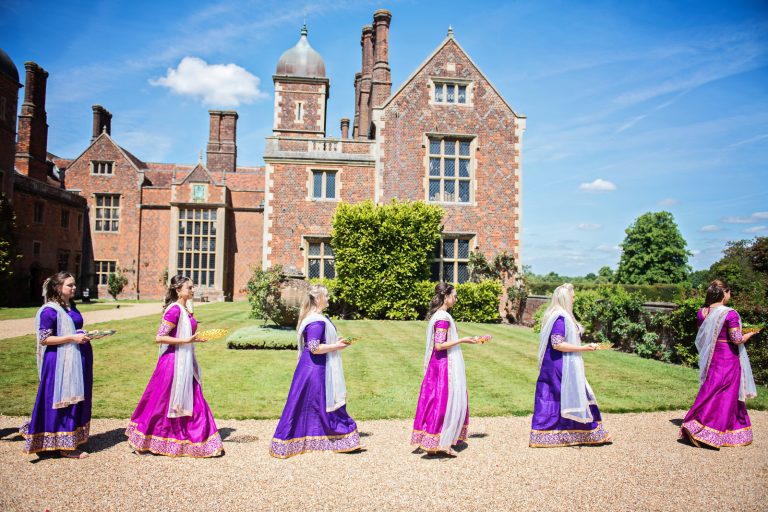 Bridesmaids in procession (arranged like the Beatles Abbey Road album), walk with gifts, during Hindu ceremony at North Mymms Park, candidly photographed by Blooming Photography.