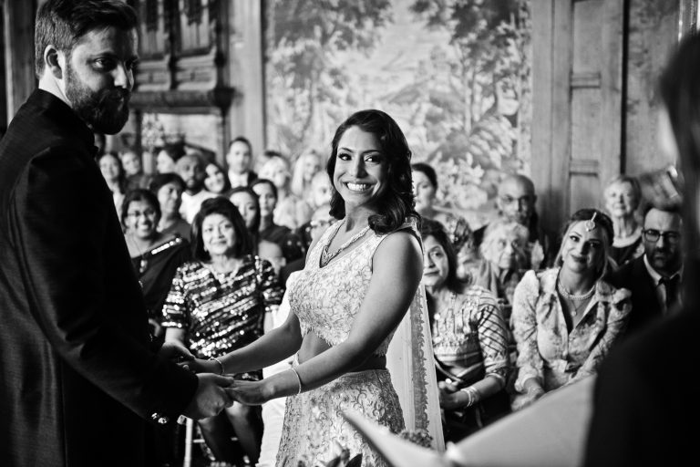 Photograph of bride and grooms holding hands during the wedding ceremony. Bride is beaming with her smile. Black and white image. Photographed at North Mymms Park, by Blooming Photography.