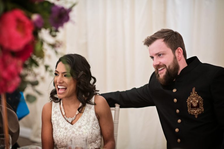 Bride and groom smiling as they listen to the father of the brides speech. Photographed at North Mymms Park, by Blooming Photography.