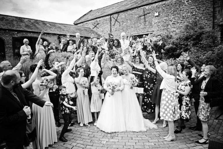 B&W photo of bride and bride celebrating with their guests with confetti at Dodmoor House.