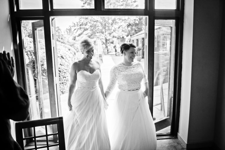 B&w photo of the bride and bride being welcomed in by their guests for the wedding breakfast.
