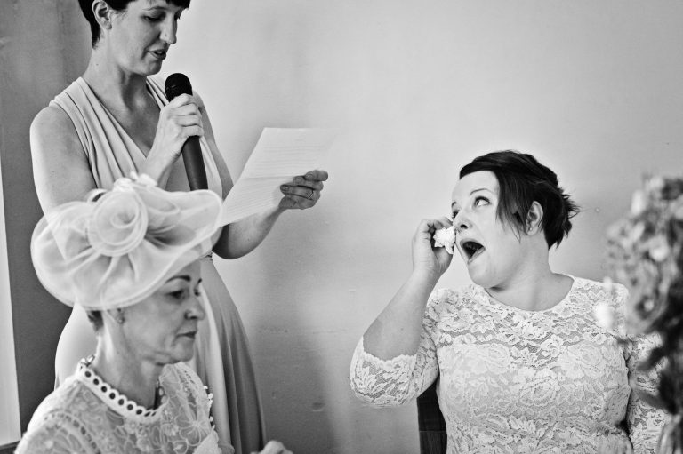 B&W storytelling photo of the brides sister delivering her speech whilst the bride is wiping tears away from her eyes.