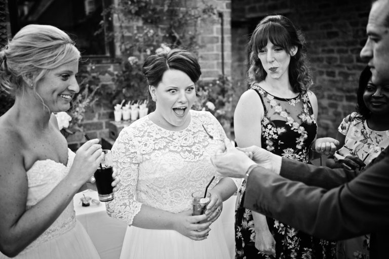 B&W documentary photo of bride and bride watching a magic trick in awe.