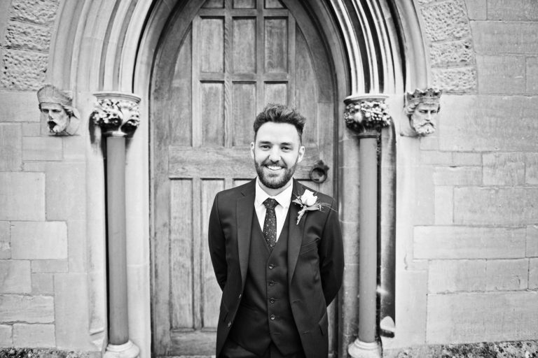 Groom poses in front of an old church door and arch before his wedding. B&W photo.