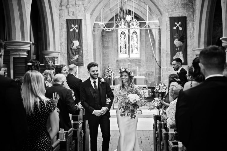 B&W candid photo of bride and groom walking down the wedding isle of the church.