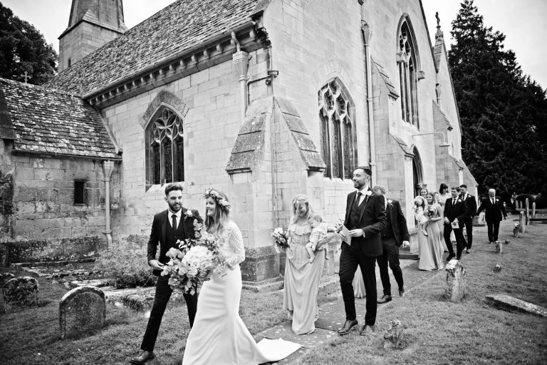 Candid photo of bride and groom leaving church with their close family behind them.