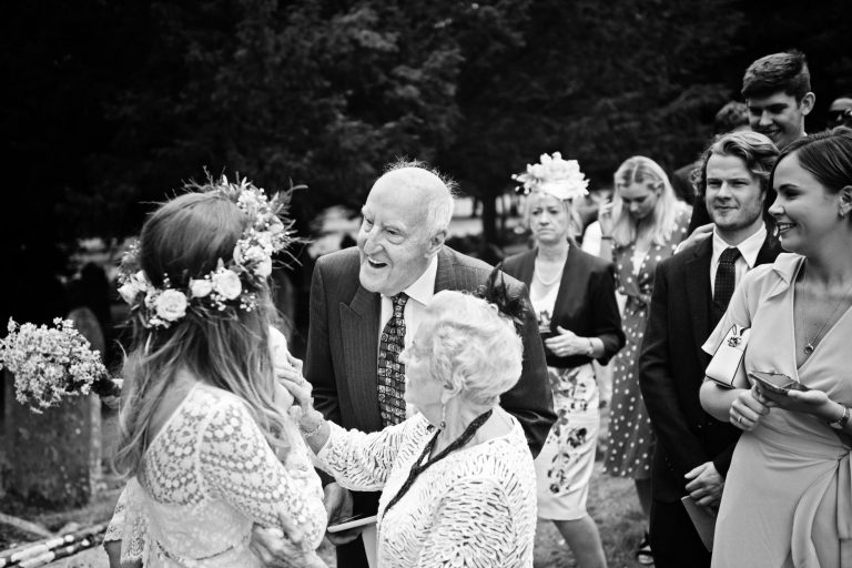 B&W candid photo of wedding guests chatting to the bride and smiling.