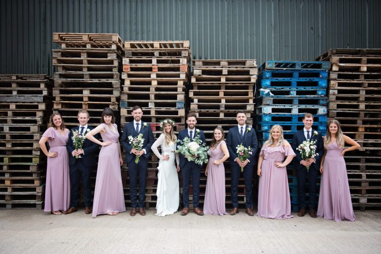 Photo of bride and groom and bridal party having fun and posing in front of wooden pallets for their wedding at Overbarn, Gloucester.
