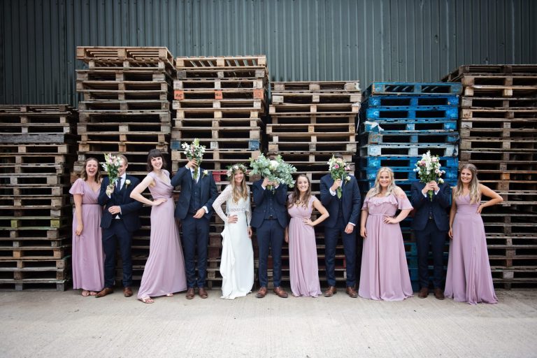 Photo of bride and groom and bridal party having fun and posing in front of wooden pallets for their wedding at Overbarn, Gloucester.