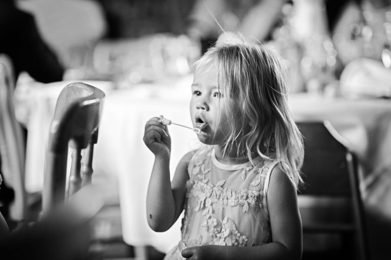 B&W photo of a young child trying to blow bubbles at a wedding at OverBarn, Gloucester. Photo by Blooming Photography.