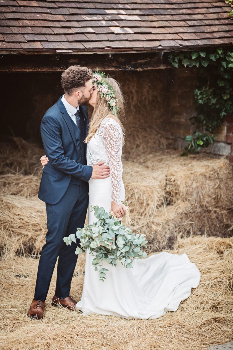 Candid photo of bride and groom kissing on a bed of straw at OverBarn wedding venue.