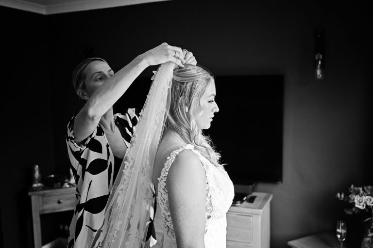 a b&w image of a bride having her veil fitted