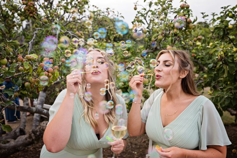 Bridesmaids blowing bubbles with apple trees behind them.
