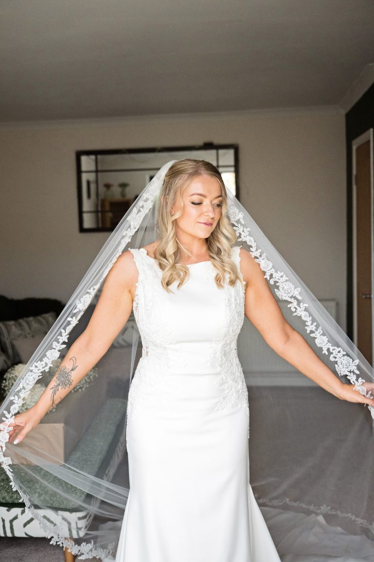a bride facing the camera adjusts her beautiful veil in a swanlike manner