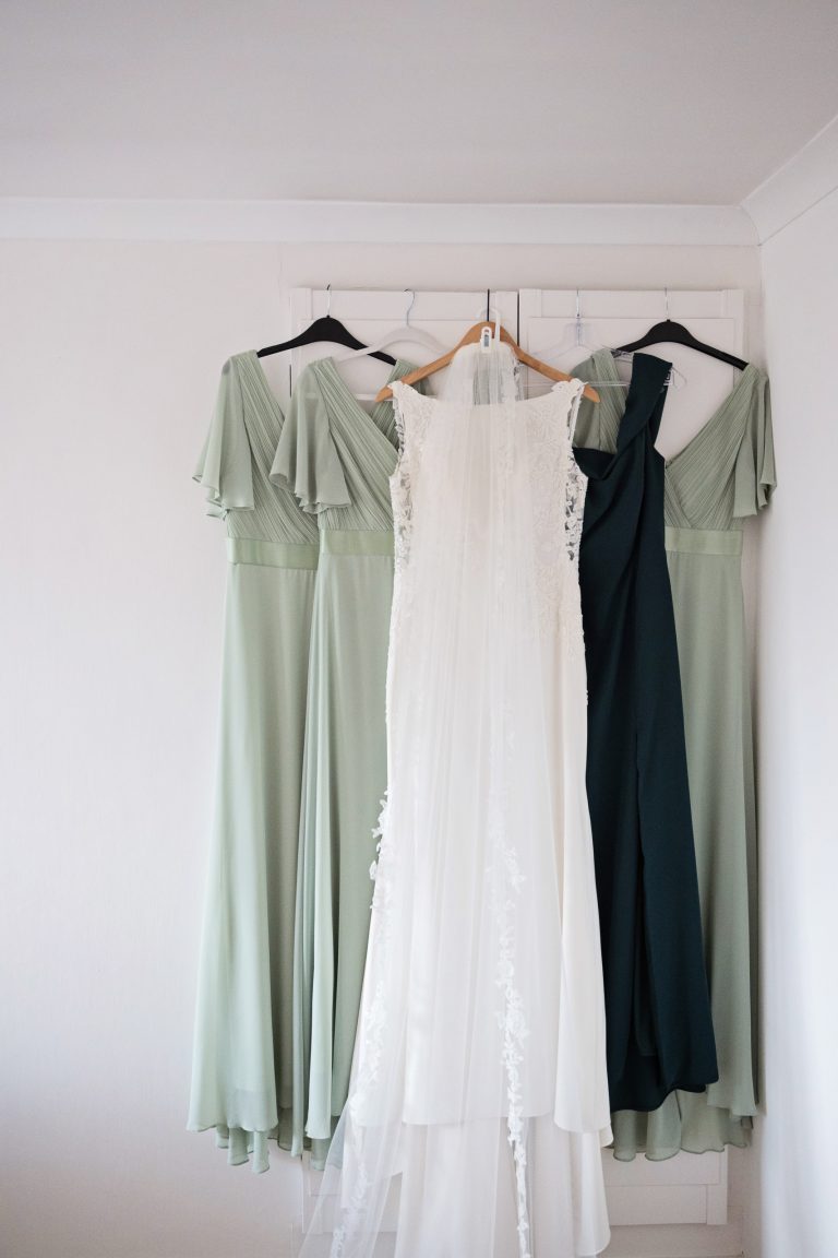 portrait image of bridesmaids dresses and a wedding dress hung up on a door