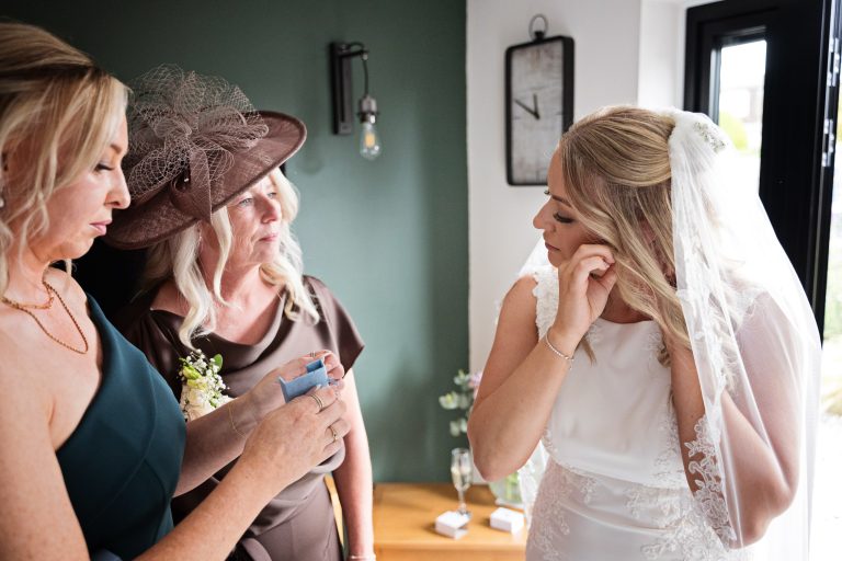 bride putting on her earings whist maid of honour and mum watch.