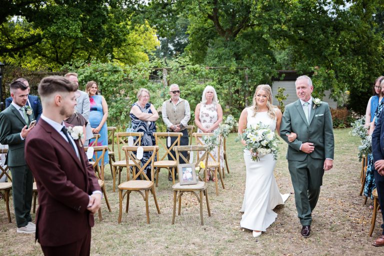 the bride and father of the bride walk down the garden wedding isle towards the groom.