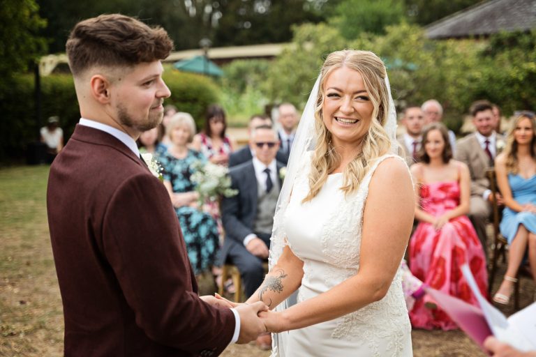 bride and groom holding hands smiling (as are their wedding guests smiling behind them)